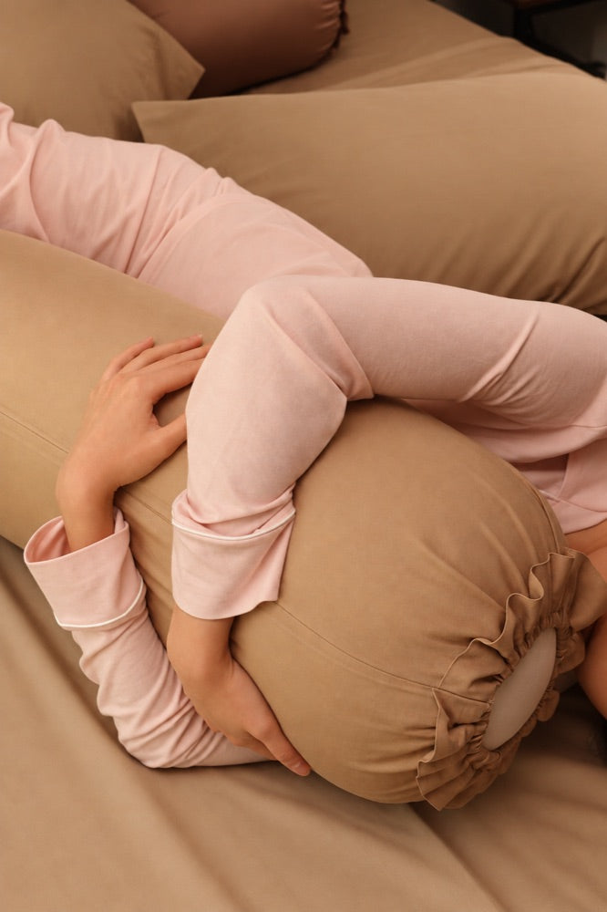 Person in pink pajamas hugging a tan Koalu body pillow in bed