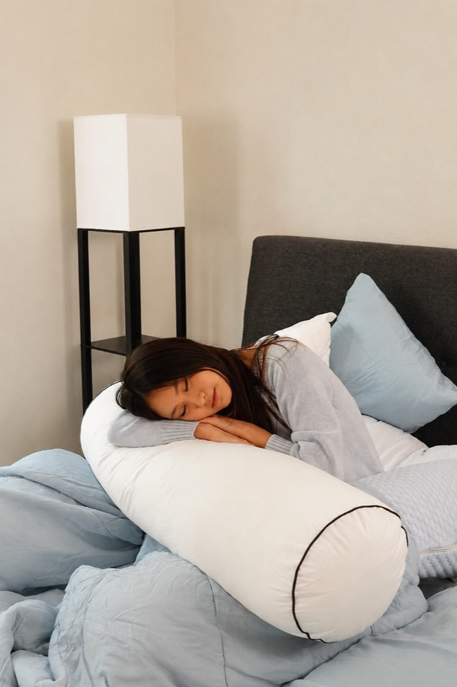 Woman resting her head on a white Koalu body pillow in bed with light blue bedding